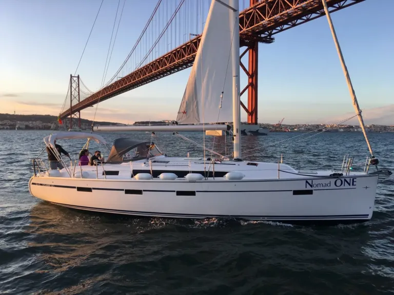 White sailboat passing beneath a suspension bridge