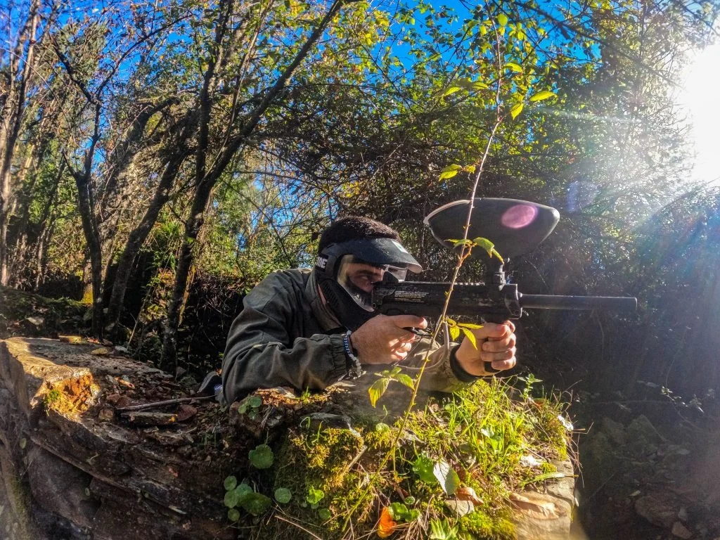 Paintball player aiming from behind a bush