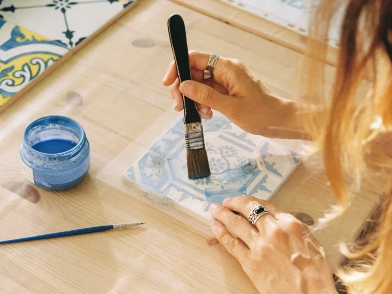 Hand painting a blue pattern on a ceramic tile