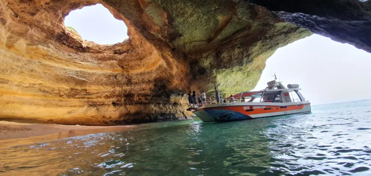 Excursion boat entering a sandstone sea cave with an open roof