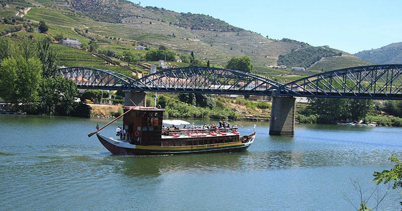 Traditional wooden cargo boat on the river beside an old iron bridge