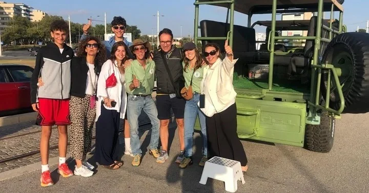 Group of visitors smiling in front of a green open-top military-style vehicle