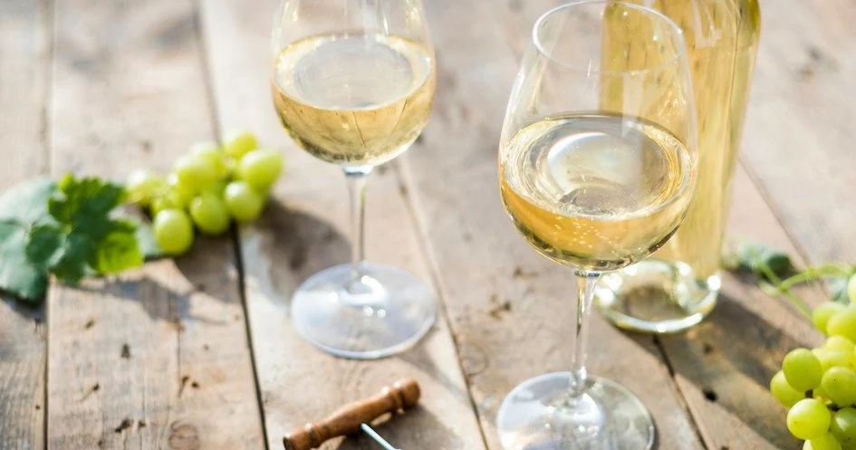 Two glasses of white wine on a wooden table beside green grapes