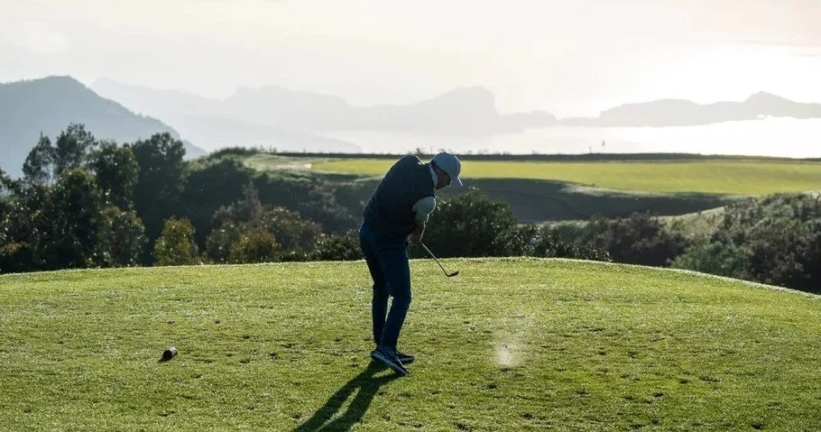 Golfer in mid-swing on a fairway overlooking green hills