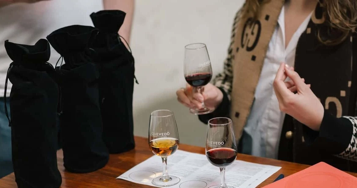 Woman tasting wine beside black bags used for a blind tasting