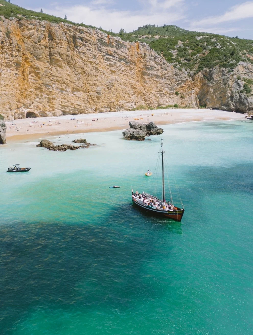 Sailing boat anchored in a turquoise cove below cliffs
