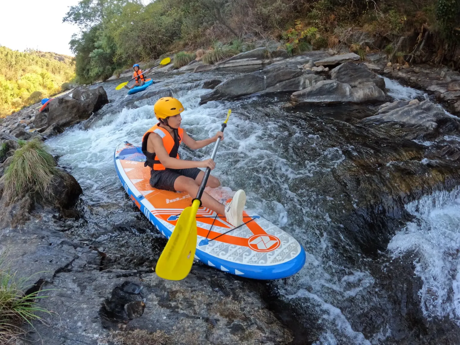 Paddler in a helmet on an inflatable paddleboard in a rocky rapid