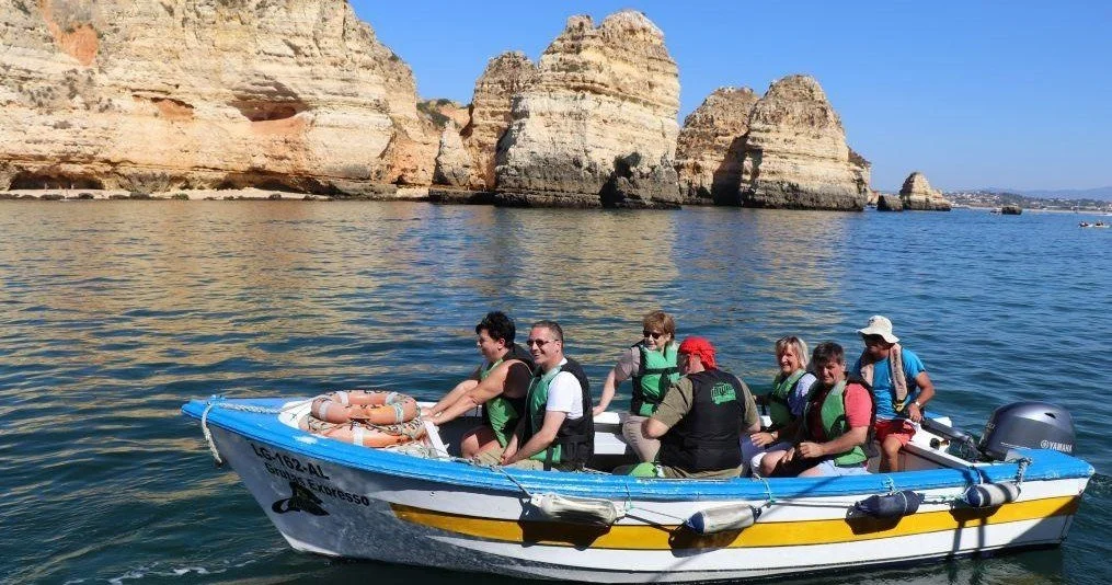 Small colourful boat with passengers in life jackets below rocky cliffs
