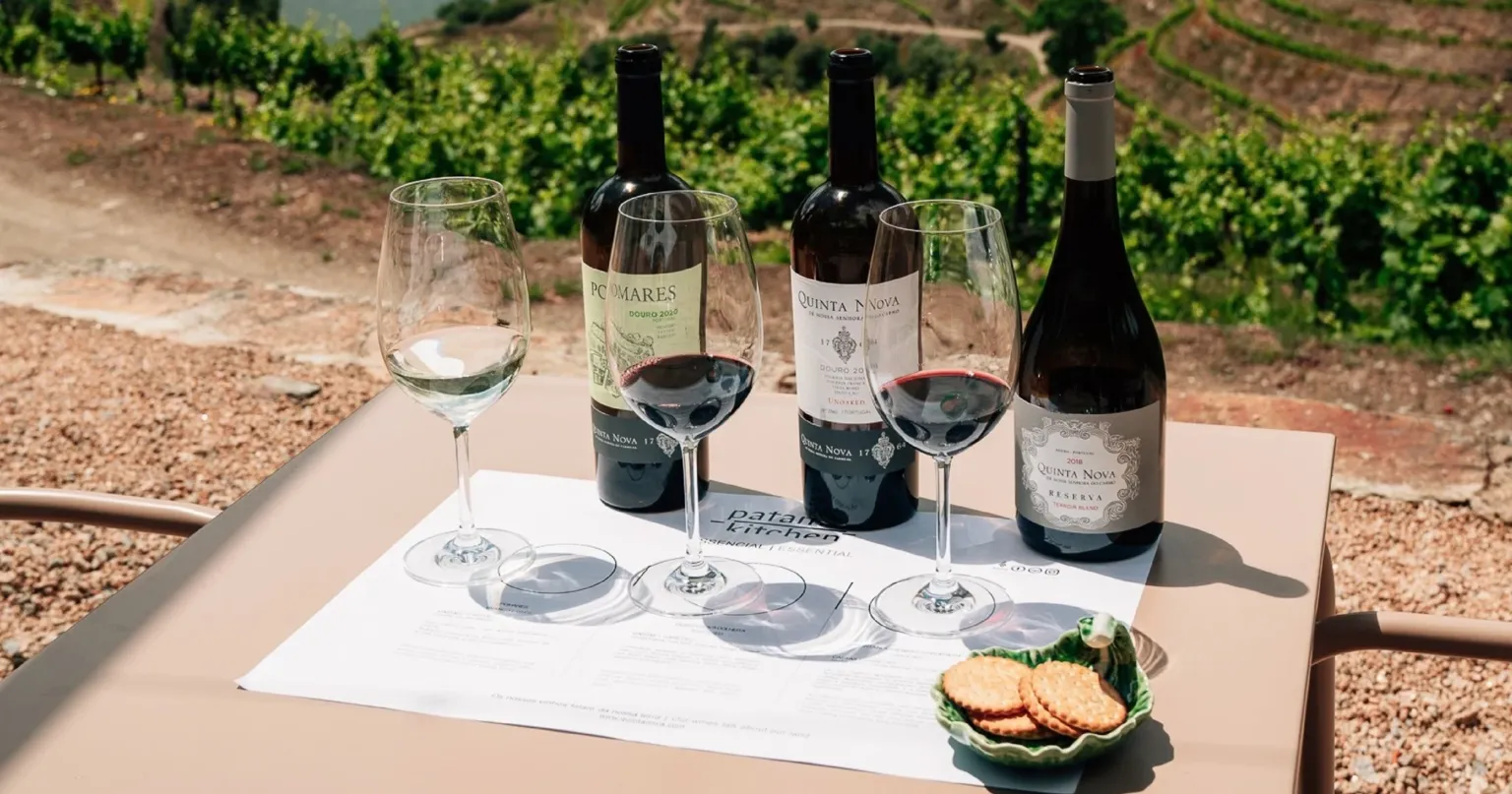 Three bottles and glasses of wine on a tasting mat with vineyard terraces behind