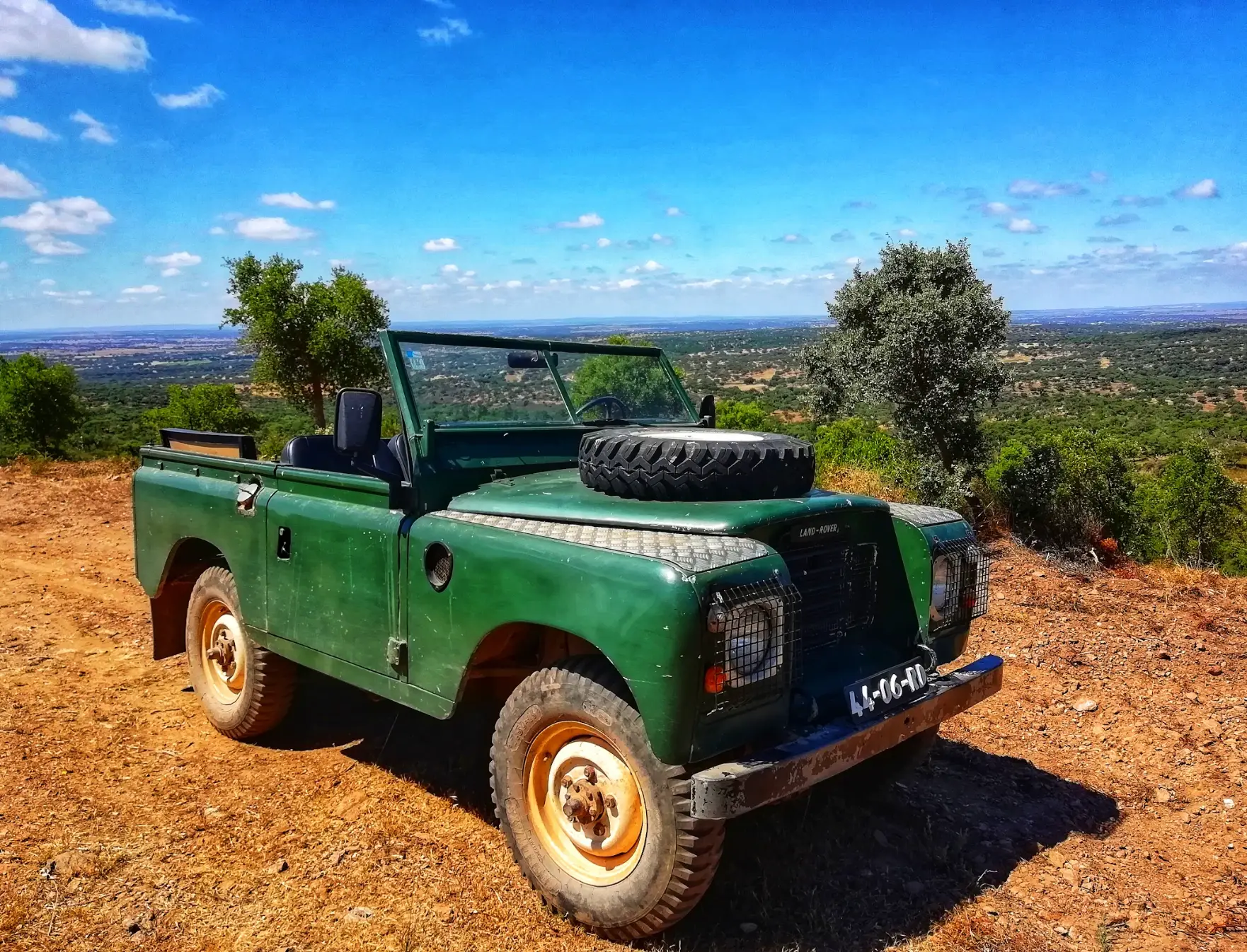 Groene klassieke Land Rover op een rode onverharde weg met uitzicht over de vlakte