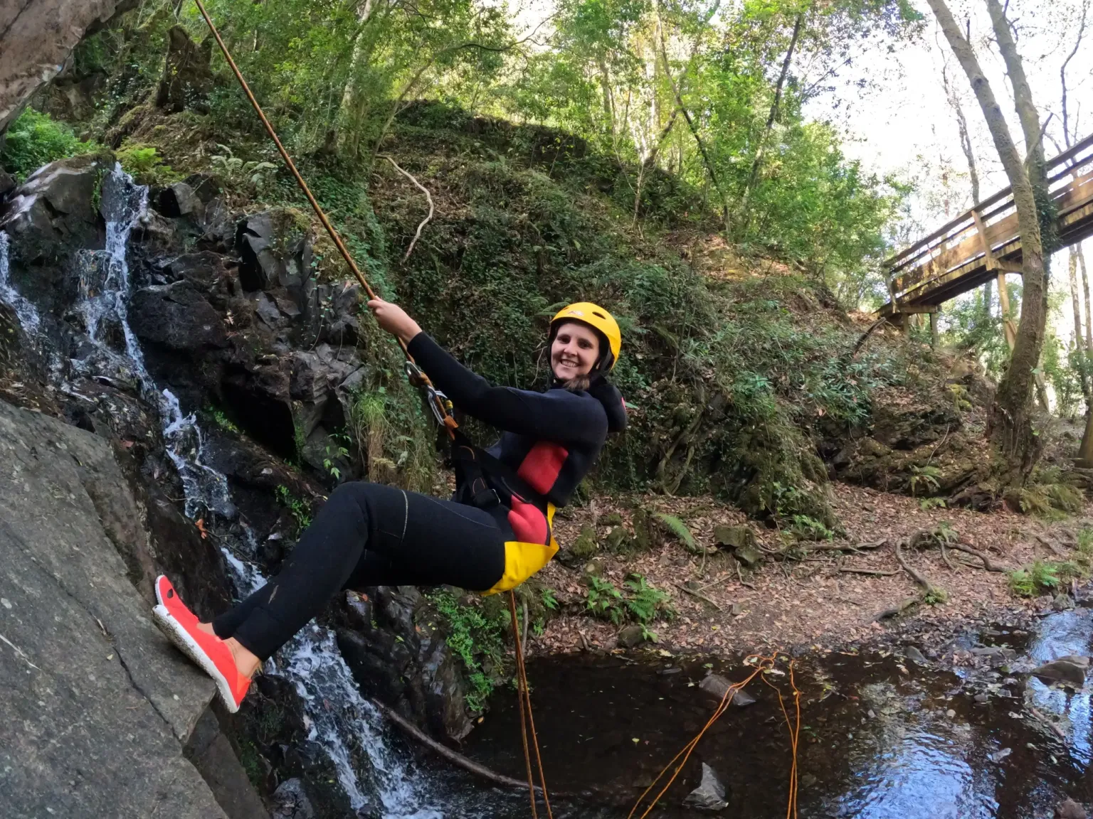 Woman in a helmet abseiling beside a small waterfall