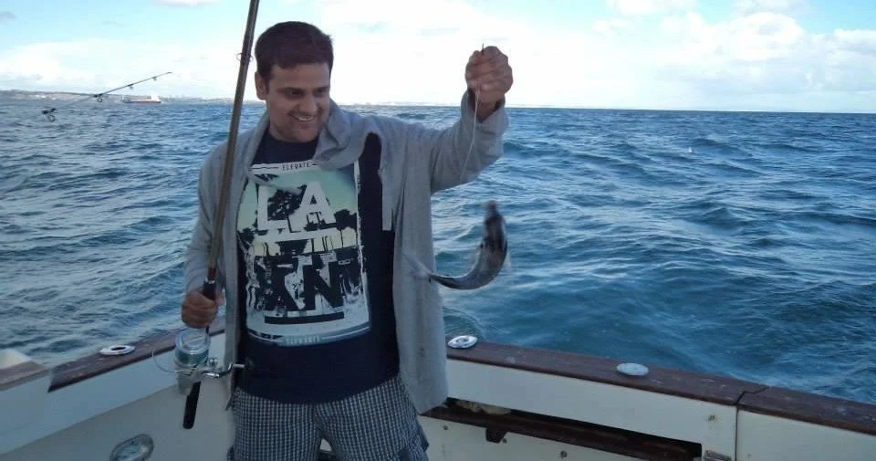Homem a segurar uma cana de pesca e um peixe a bordo de um barco