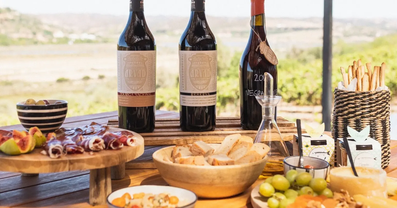 Wine bottles and a spread of charcuterie and bread on a table above vineyards