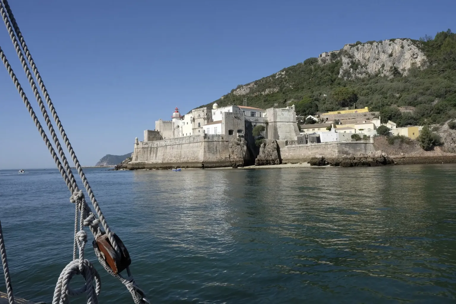 Whitewashed fortified buildings on a headland seen from a sailing boat