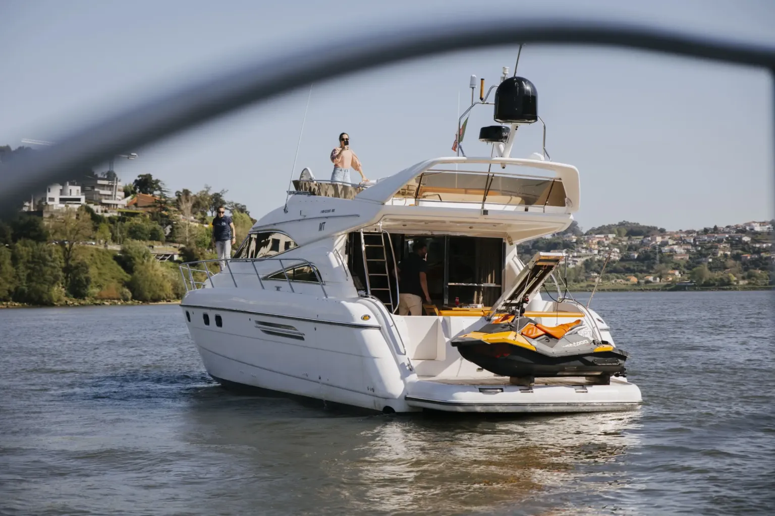 White motor yacht with a jet ski on its stern cruising the river