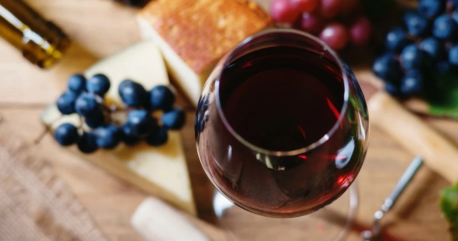 Glass of red wine on a board with cheese and grapes