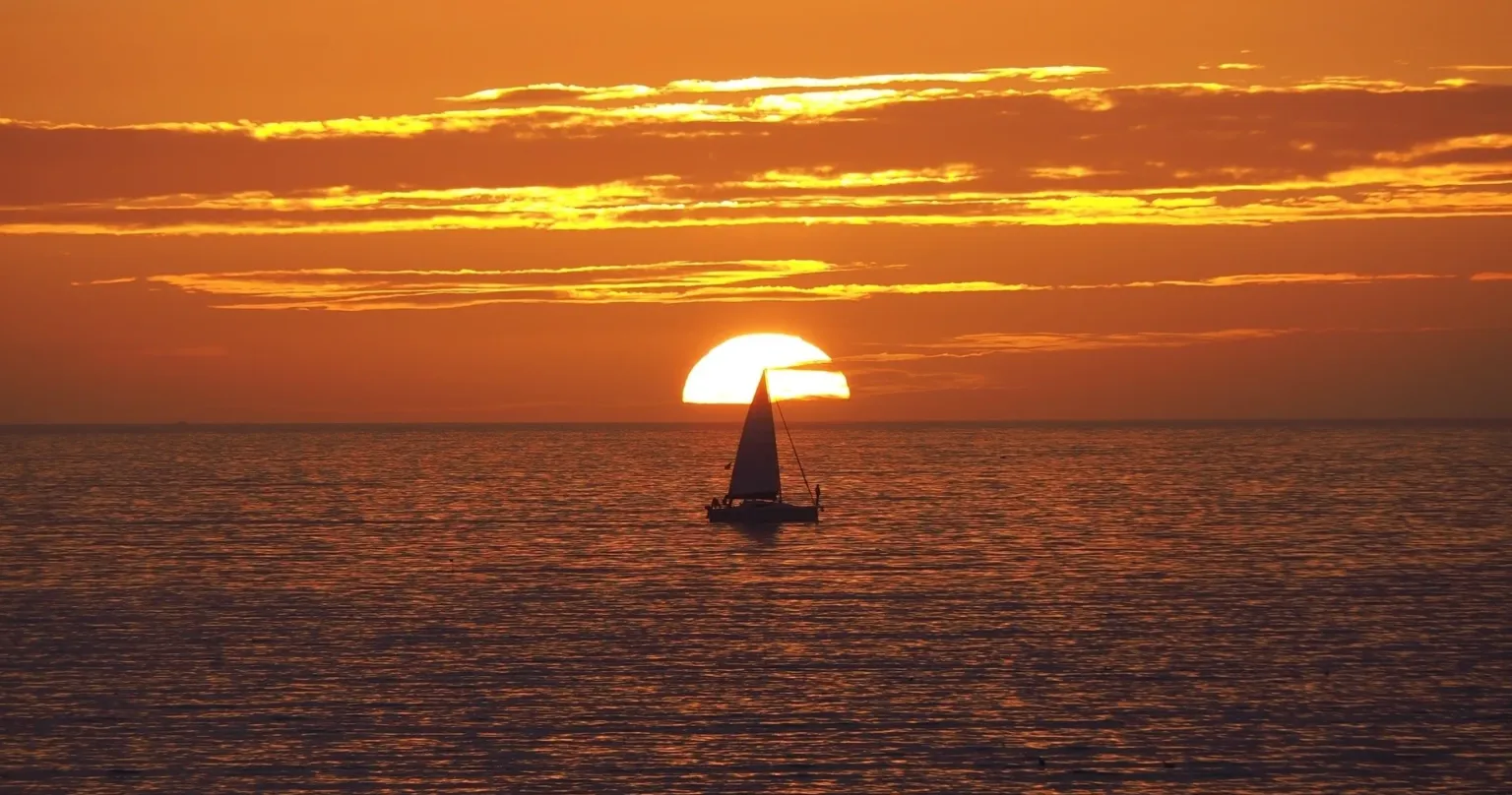 Sailboat silhouetted against a setting sun on the horizon