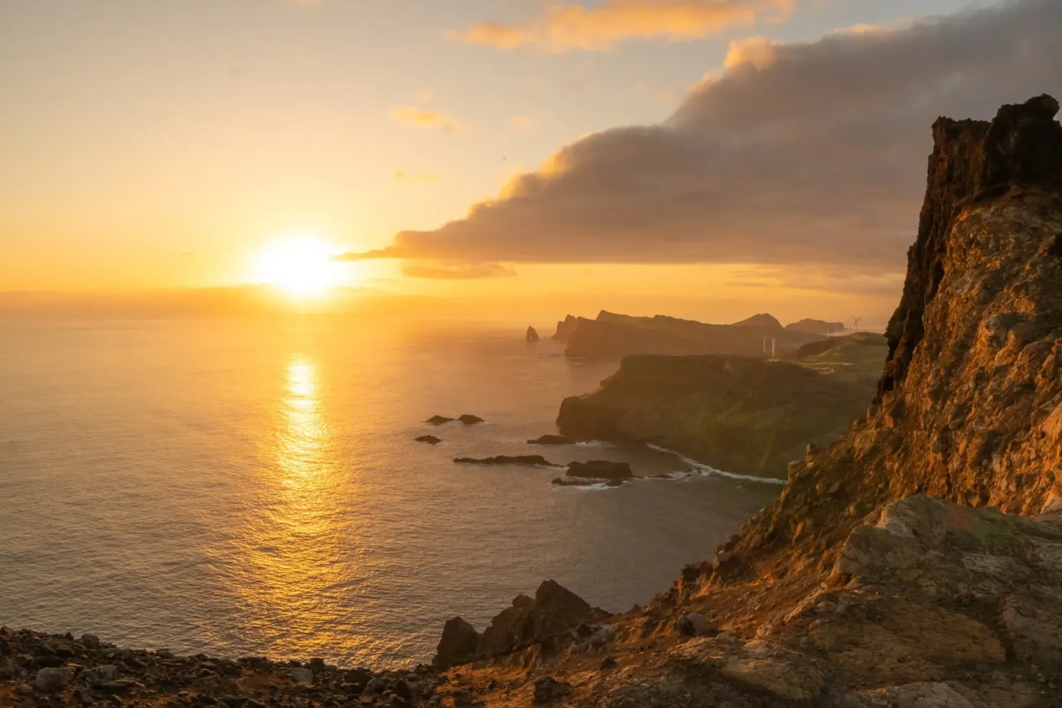 Sun rising over the sea beyond rugged coastal cliffs