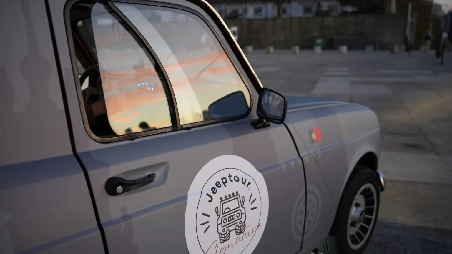Side of a small grey vintage car with a Jeeptour logo on its door