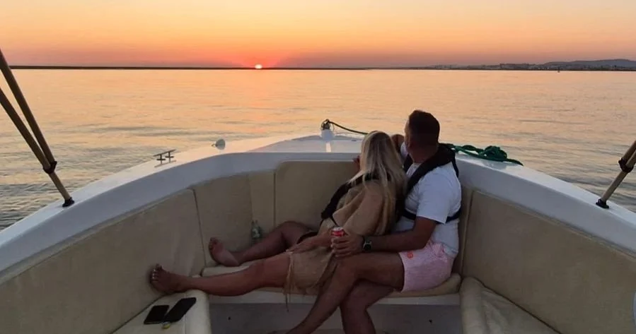 Pareja descansando en la proa de un barco al atardecer
