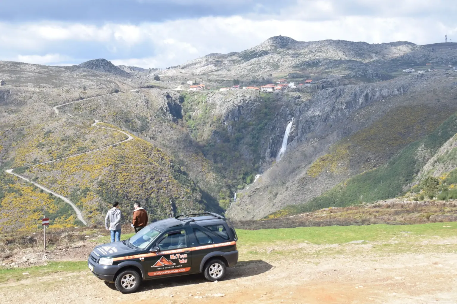 Black 4x4 parked in front of a mountain valley with a waterfall