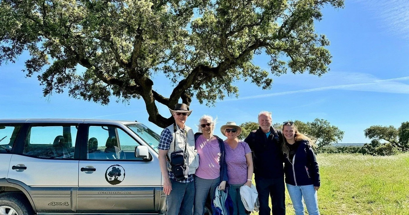 Grupo de visitantes sonrientes junto a un 4x4 plateado bajo un alcornoque
