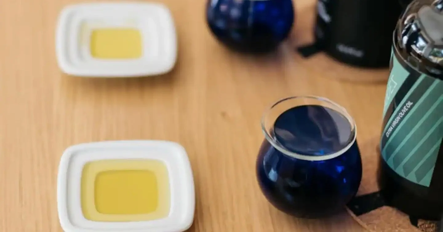Small dishes of olive oil and a blue tasting glass on a wooden table