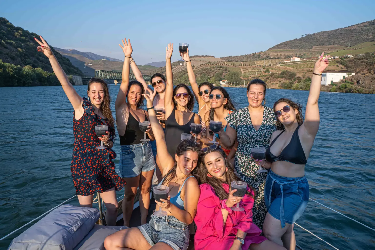 Group of women raising wine glasses and arms on a boat deck on a river