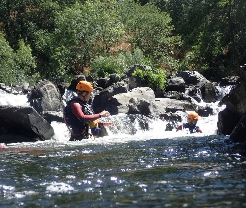 Participants in helmets wading through rapids between boulders