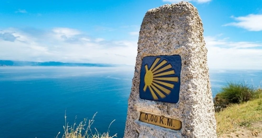 Stone Camino de Santiago marker with a shell symbol and '0,00 km' above the sea