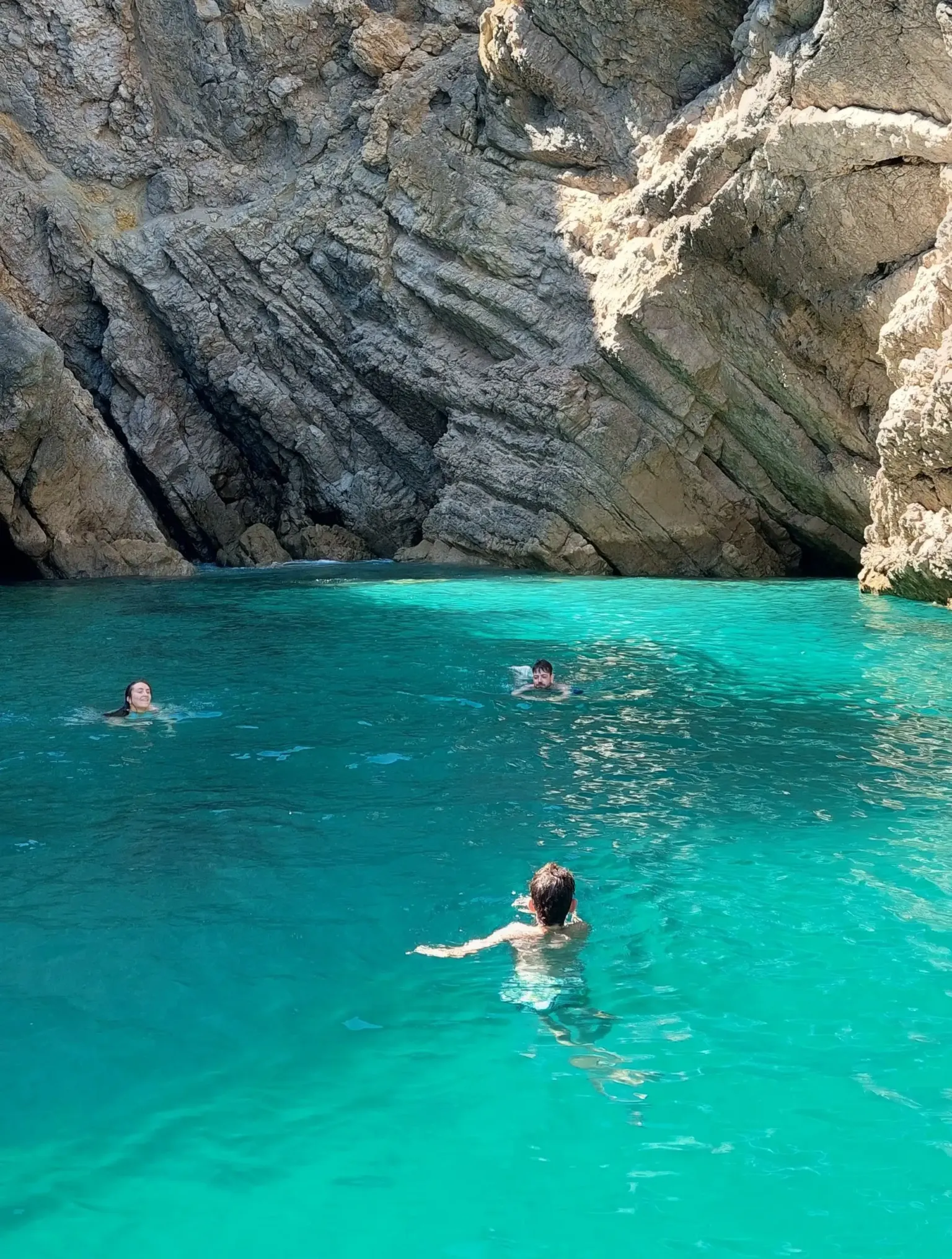 Swimmers in turquoise water at the foot of a grey cliff