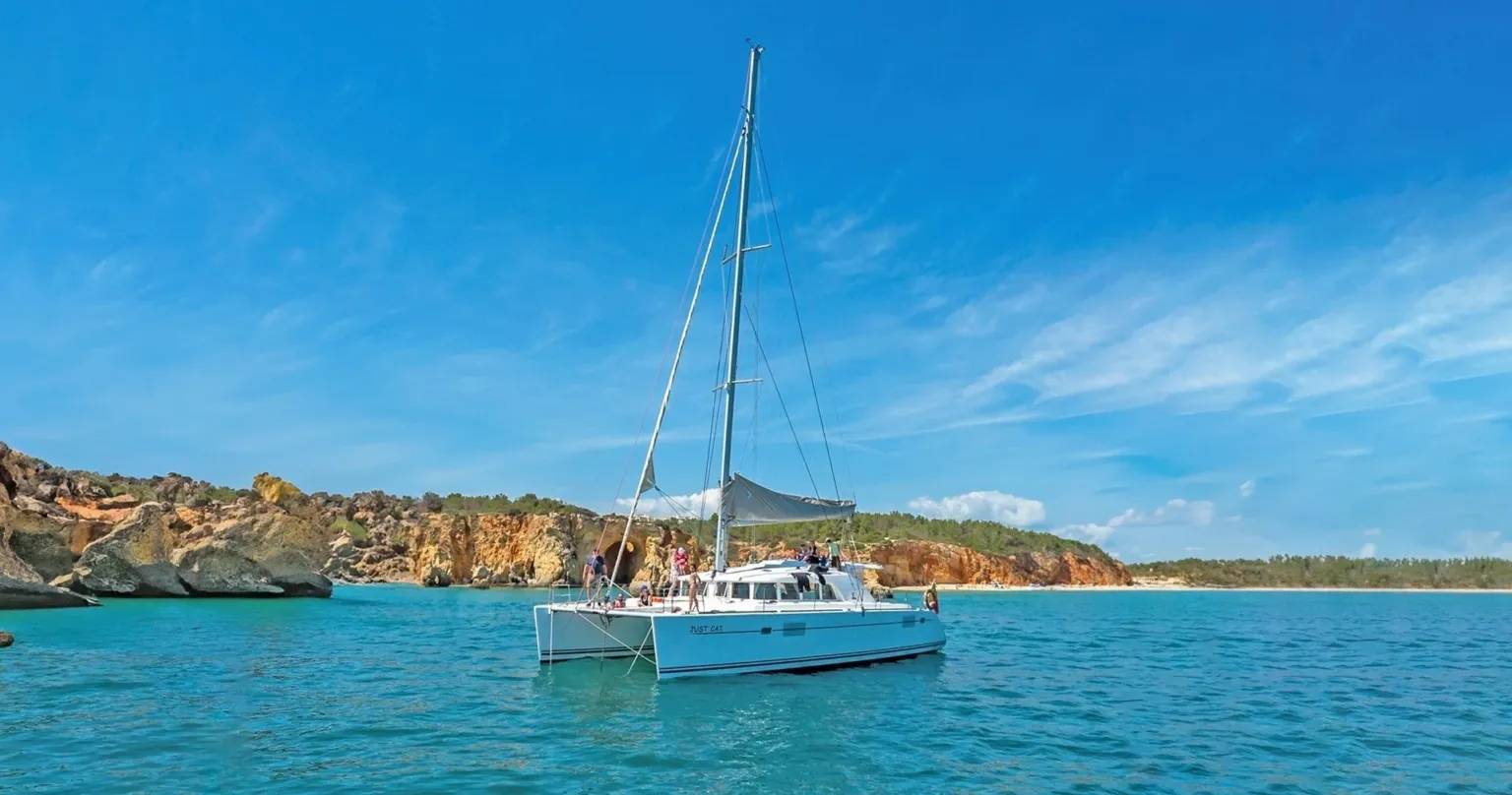 Catamaran at anchor off a rocky coast under a blue sky