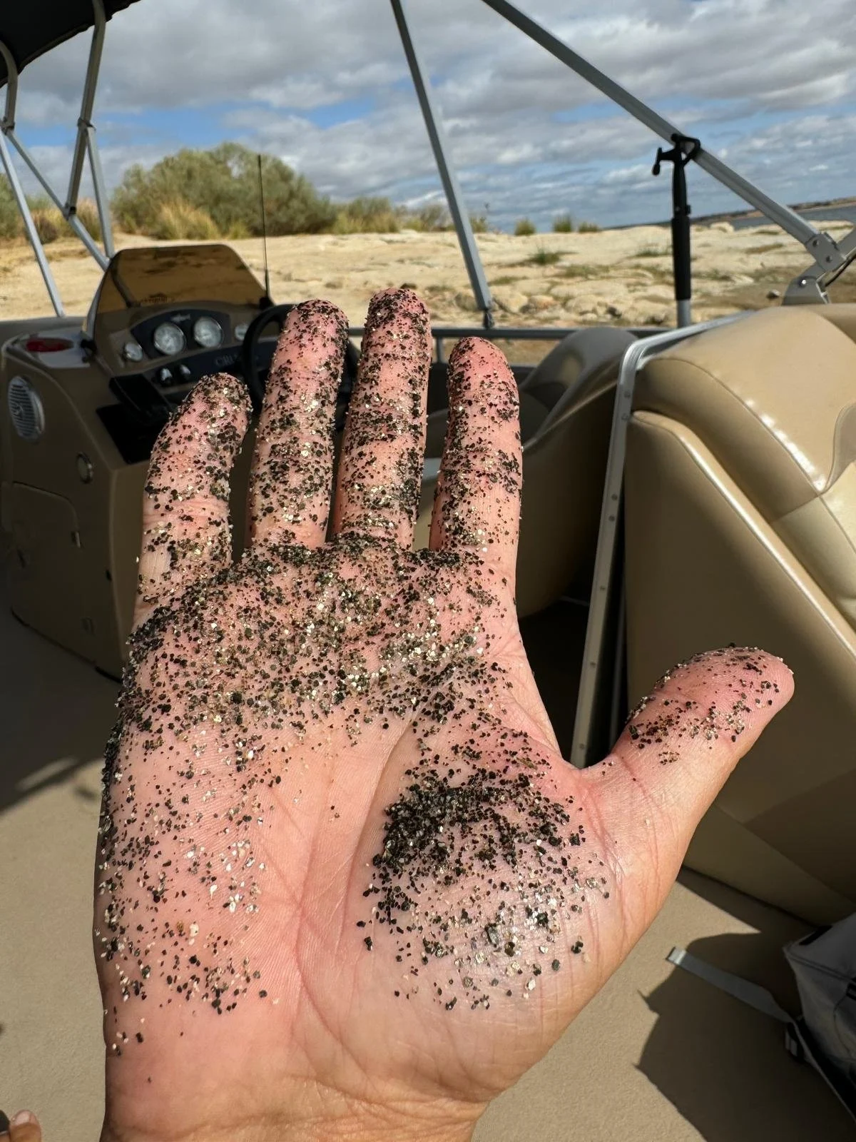 Hand dusted with dark sand beside a boat's steering console