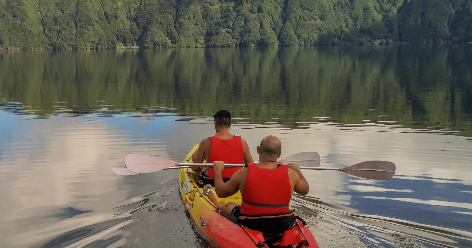Two kayakers paddling on a calm forest lake