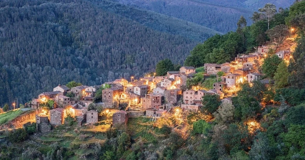 Schist village lit up at dusk on a forested mountainside