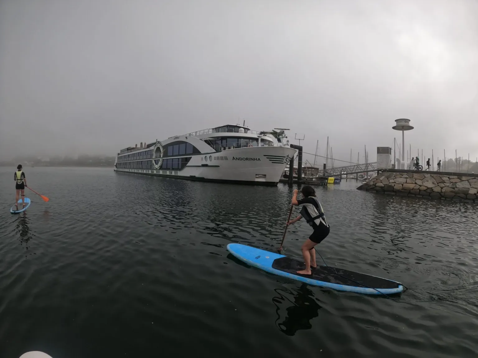 Paddleboarder on a misty river with a cruise ship moored behind