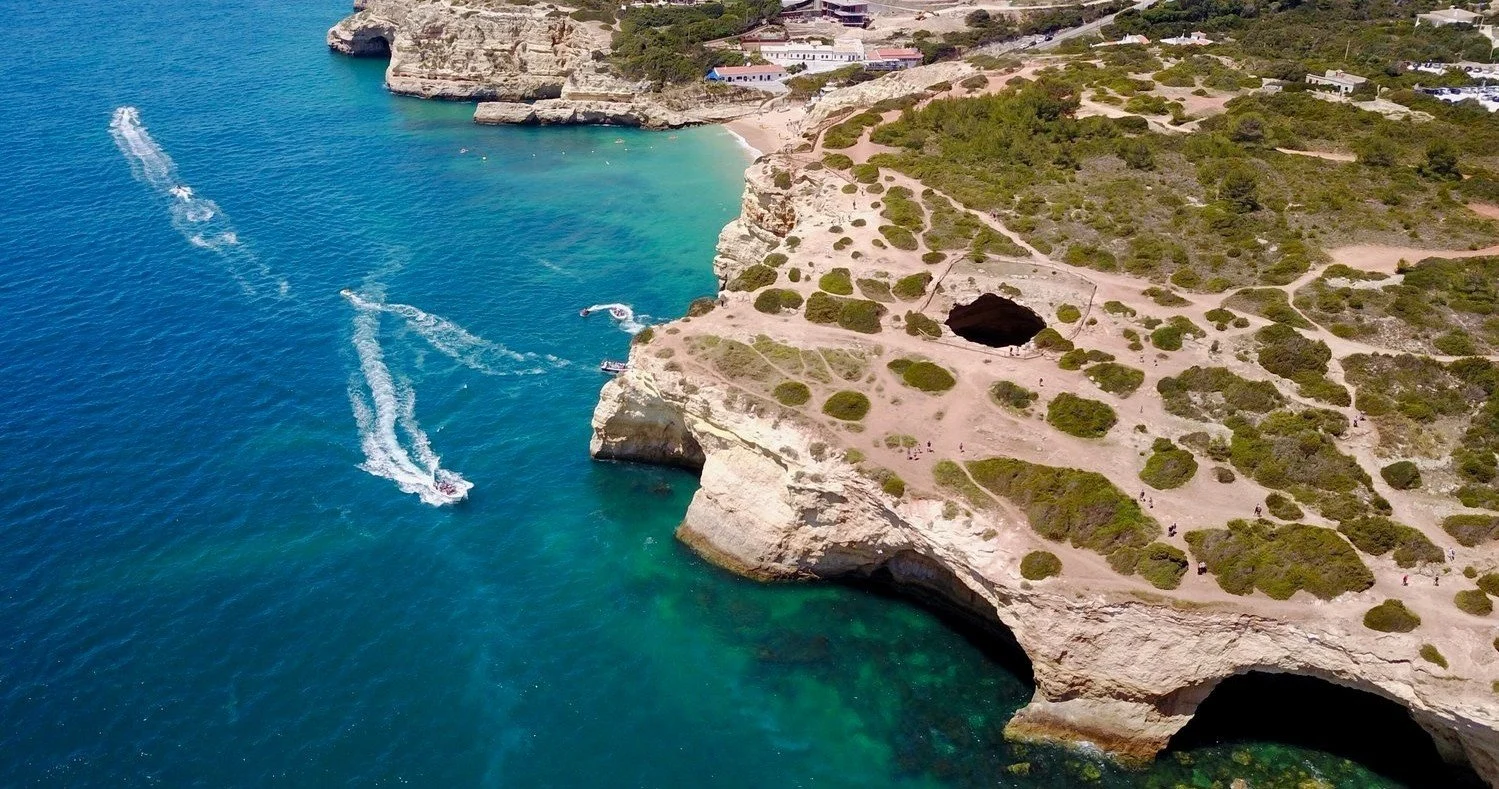 Aerial view of a speedboat leaving a wake beside a cliff-lined coast with cave entrances
