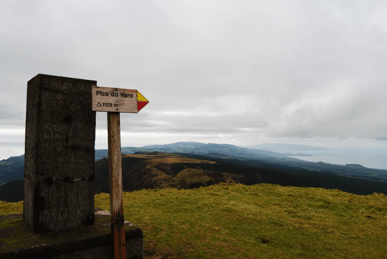 Signpost on a hilltop with views of distant islands under cloud