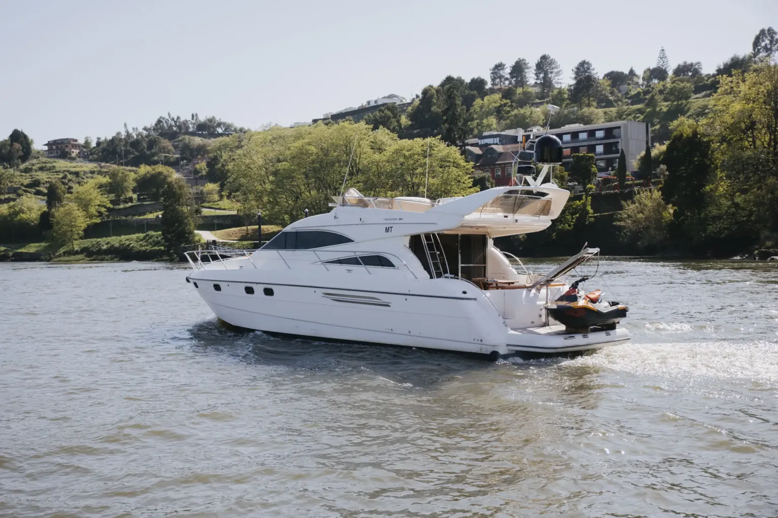 Motor yacht with a jet ski on its stern on a river with wooded banks