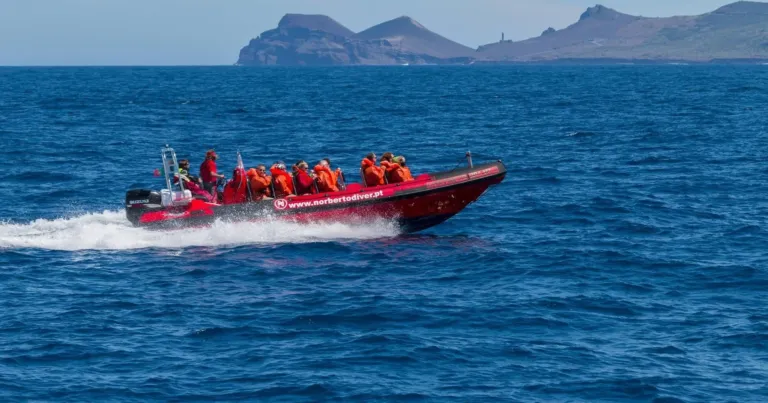 Red rigid boat full of passengers speeding across the sea