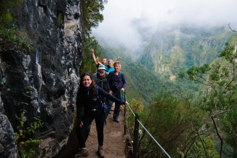 Hikers on a narrow path cut into a rock wall above a misty valley