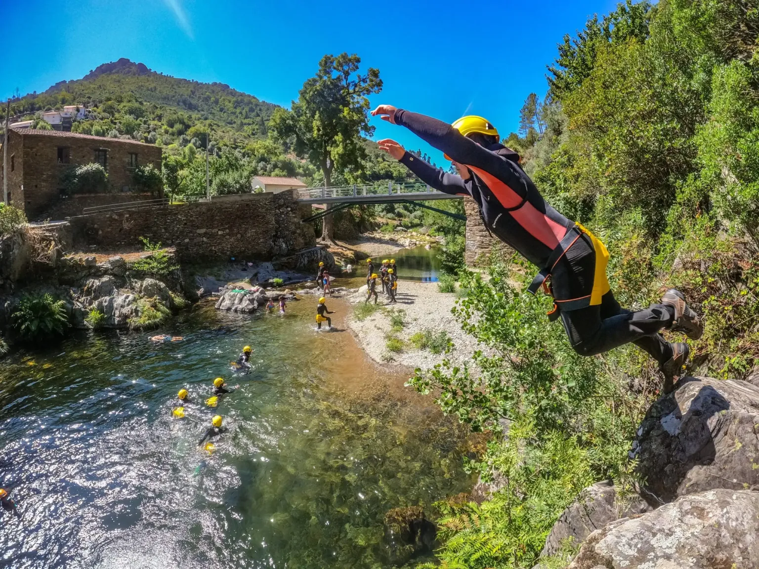 Person in a wetsuit leaping from a rock into a river