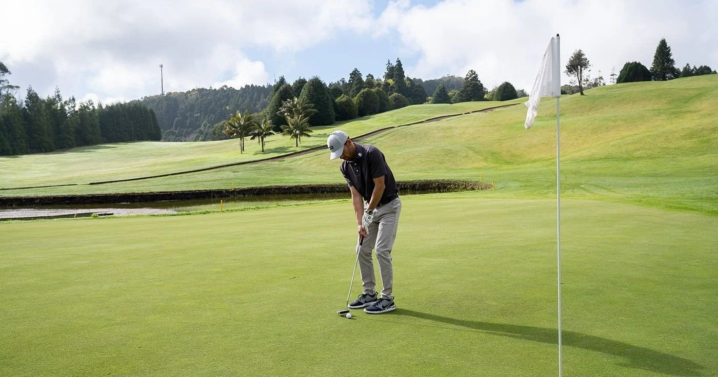Golfer putting on a green beside the flag among trees