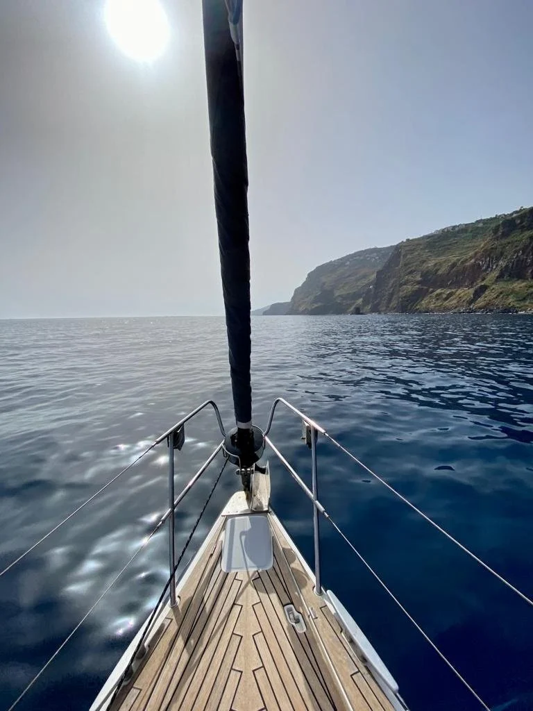 Wooden foredeck of a sailboat pointing towards a coastal cliff