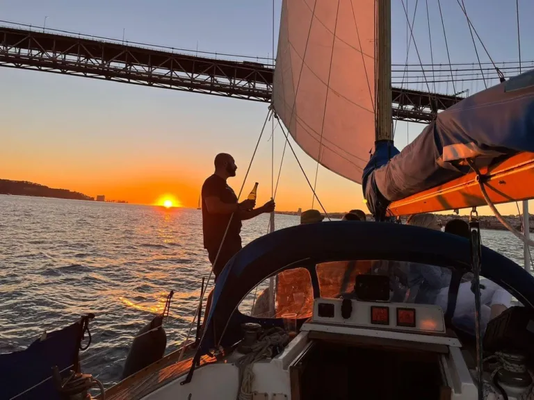 Skipper silhouetted against the sunset beneath a bridge, seen from a sailboat