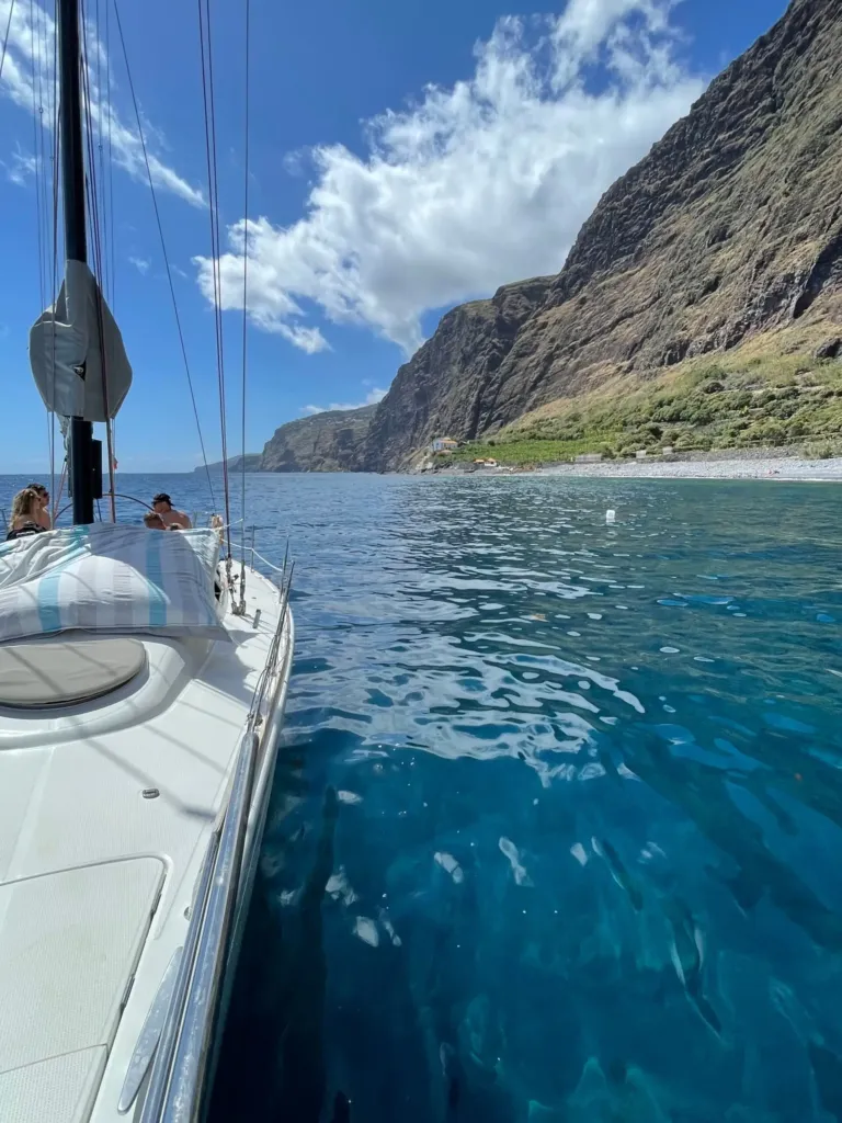 Side of a sailboat and sea cliffs rising beside the water