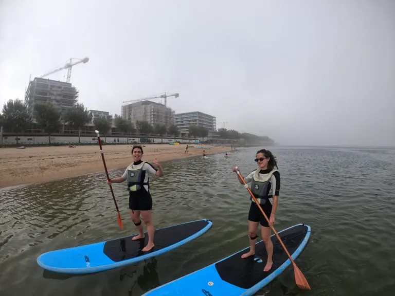 Two paddleboarders on a misty estuary near a beach