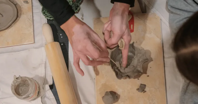 Hands shaping clay on a wooden board