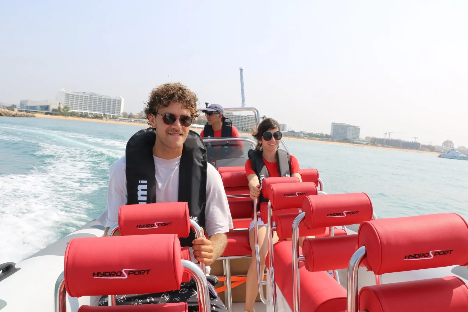 Man and woman on red seats of a fast rigid boat with a beach resort behind