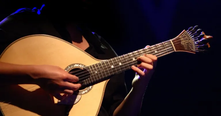 Hands playing a Portuguese guitar on a dark stage